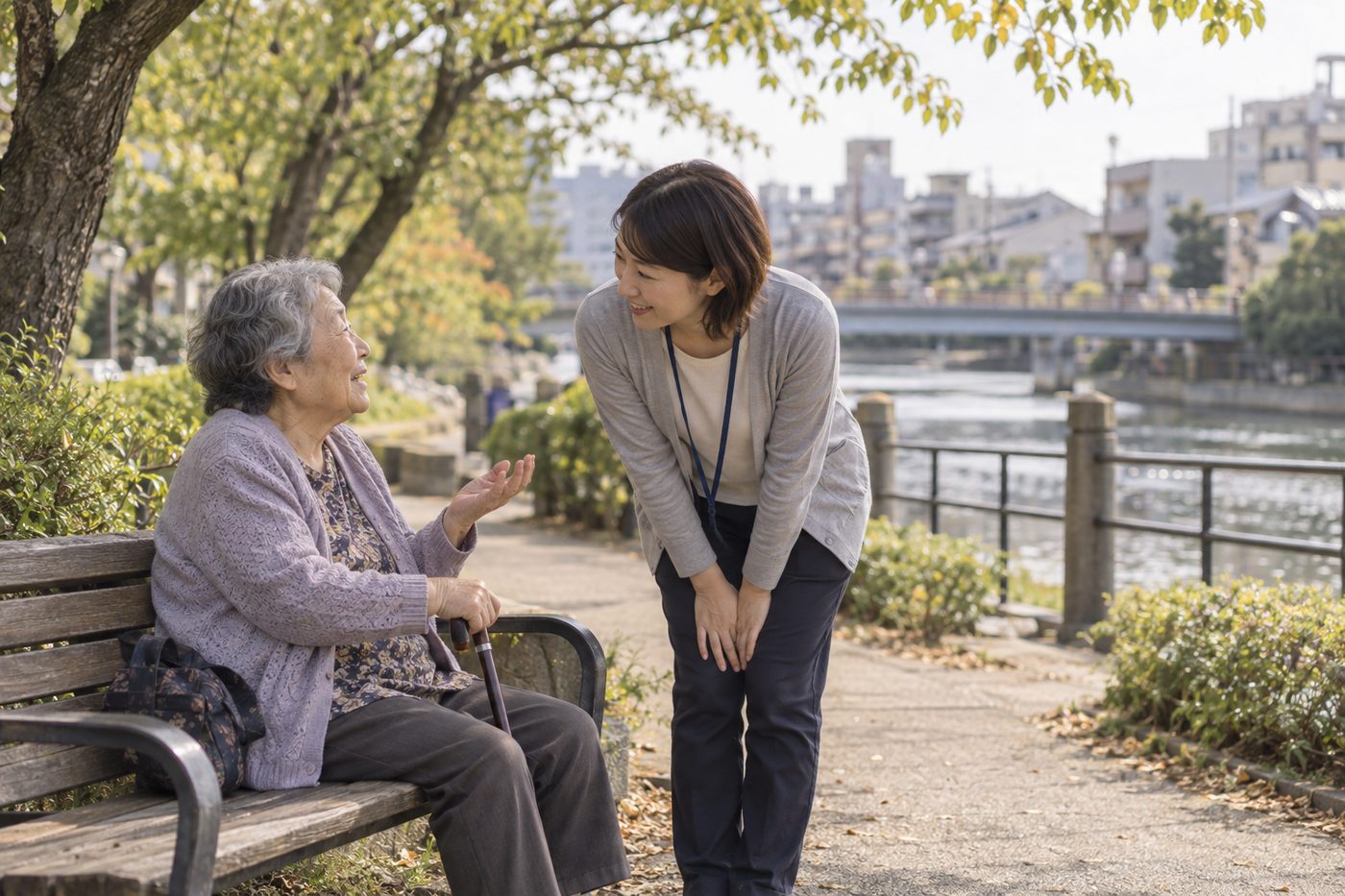 川沿いのベンチで、職員が高齢の女性の話を聞いている様子